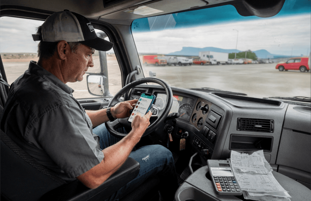 Owner-operator reviewing dispatch messages on a smartphone inside a truck cab