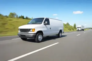 A white cargo van running at speed on an open interstate highway